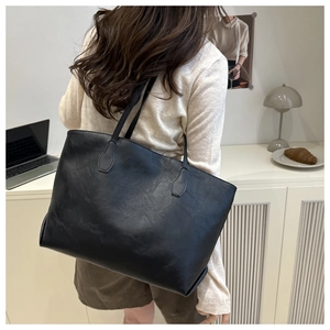 Minimalist large black tote bag shown on model in a cozy, warm home office setting
