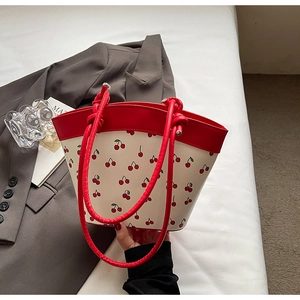 Detail of red cherry print bag with woven rope handles and leather trim on grey blazer
