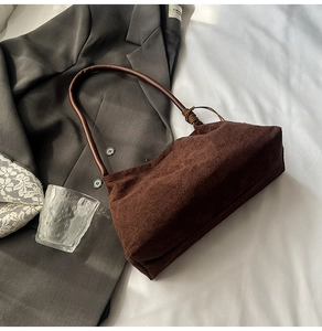Detail of dark coffee suede shoulder bag with unique knotted strap on grey blazer fabric