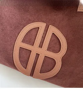 Macro shot of circular faux leather logo and fine stitching on a suede retro tote bag