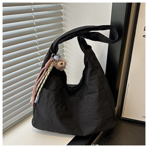 Detail of black crescent nylon tote bag with plush charm on window sill in natural light