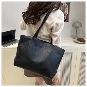 Practical large black faux leather tote bag worn by a model in a cozy indoor setting