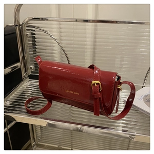 Detail of red patent leather crossbody bag with gold buckle and glossy texture
