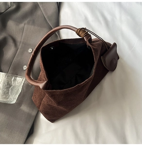 Detail of dark brown suede shoulder bag with leather circular handle and magnetic closure