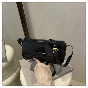 Detail of black patent leather shoulder bag with gold logo and adjustable strap