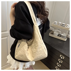 Detail view of a beige minimalist nylon shoulder bag with side pocket on a model