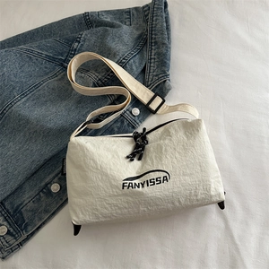 Minimalist beige nylon crossbody bag with black logo and adjustable strap on denim background
