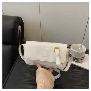 Detail of white patent leather shoulder bag with gold logo and adjustable strap