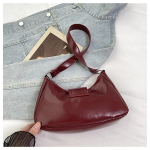 Close-up of a burgundy wrinkled leather shoulder bag on a casual denim jacket background
