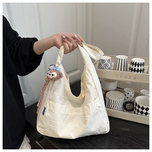 Detail of a cream nylon shoulder bag with soft pleated texture and a plush bear pendant