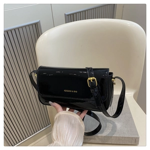 Detail view of black patent leather shoulder bag with gold buckle and adjustable strap