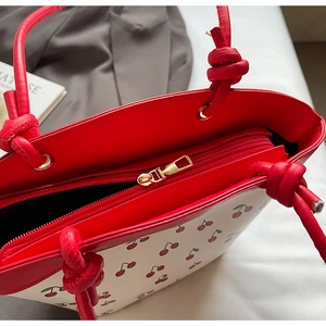 Detail of red cherry print tote bag featuring contrast colors and gold zipper closure