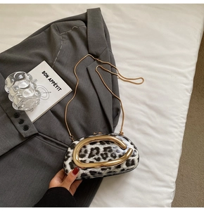 Close-up of leopard print round bag with golden metal handle and chain strap on grey suit