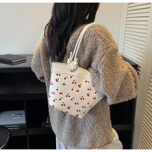 Detail view of white cherry print bucket bag featuring elegant knotted shoulder straps