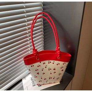 Detail shot of white tote bag with red cherry print and decorative knotted handles