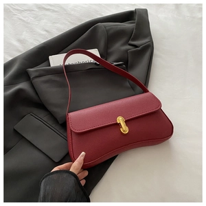 Detail of red lychee textured leather baguette bag with a golden U-shaped metal buckle