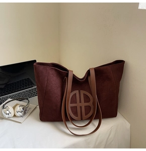Detail of burgundy suede tote bag featuring a circular cutout logo and slim leather straps