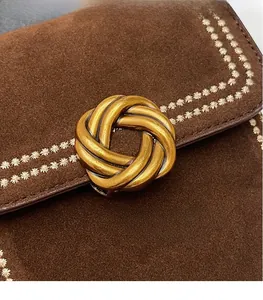 Close-up of brown suede bag featuring white floral embroidery and a golden twist metal clasp