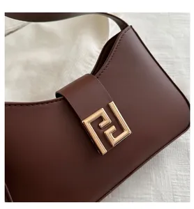Detailansicht der dunkelbraunen Lederstruktur und goldenen Metallschnalle der Tasche