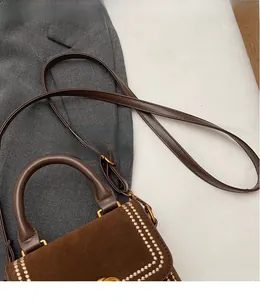 Detail of dark brown suede handbag with metal handle and golden double-G logo buckle