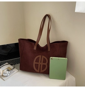 Large suede tote bag with leather logo detail next to a laptop and tablet for work