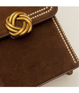 Detailed close-up of dark brown suede bag with gold twist lock and white embroidery lines