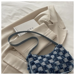 Détail du sac en toile à damier bleu et blanc avec bords effilochés sur un blazer