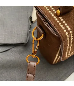 Detail of premium gold-toned metal hooks and white stitching on a brown suede crossbody bag