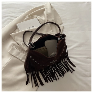 Close-up of brown suede crossbody bag with metal rivets and bohemian fringe details