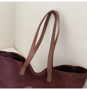 Close-up of burgundy suede tote bag showing leather strap stitching and matte texture