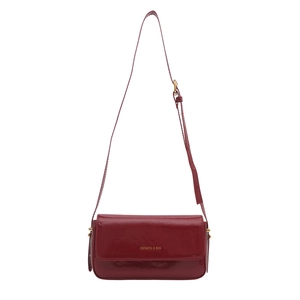 Deep red patent leather crossbody bag with gold hardware and flap closure on white backdrop