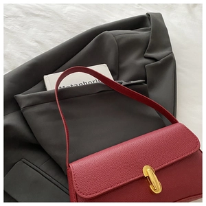 Detail of red lychee textured leather baguette bag with elegant golden capsule lock closure