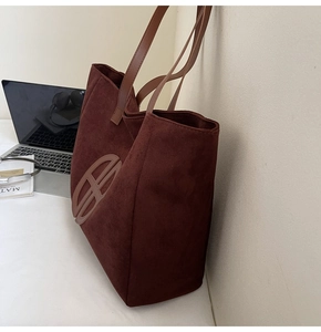 Detailed close-up of dark brown suede tote bag with leather straps on a workspace desk