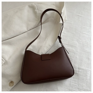 Nahaufnahme einer dunkelbraunen Leder-Achseltasche mit geschwungenem Design auf Stoff
