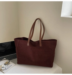 Detailed view of burgundy suede tote bag with brown leather handles in a workspace