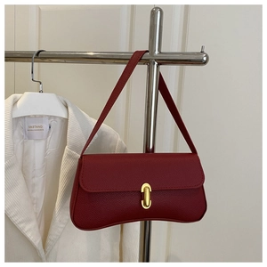 Detail of burgundy pebbled leather handbag with gold metal clasp on a textured background