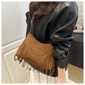 Detail of brown suede crossbody bag featuring metal rivets, cross pendant and long tassels
