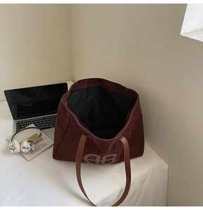 Detailed view of dark brown suede tote bag with embossed EB logo and leather handles