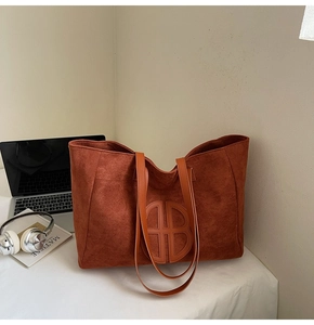 Close-up of rust red suede tote bag featuring a circular stitched logo and flat shoulder straps