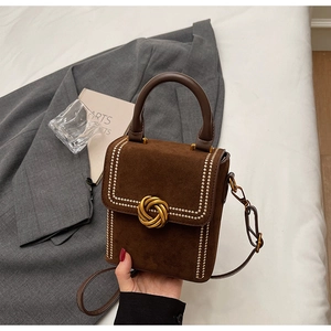 Détail du sac en daim marron foncé avec boucle nœud dorée et bords cloutés