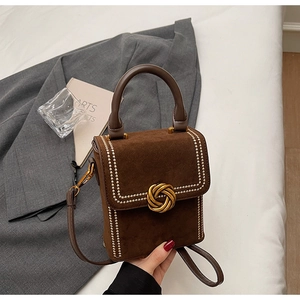 Détail d'un sac bandoulière en daim marron avec rivets dorés et fermoir métallique