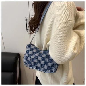 Détail du sac à bandoulière en denim à damier avec franges porté sur un pull en maille