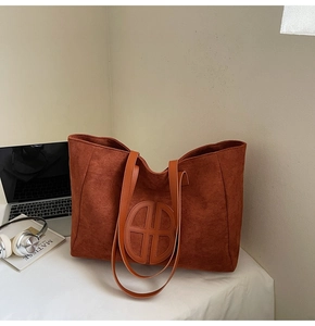 Detail of caramel suede tote bag with circular logo and long straps for daily commute