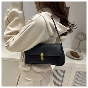 Close-up of minimalist black pebbled leather underarm bag with gold oval metal buckle lock
