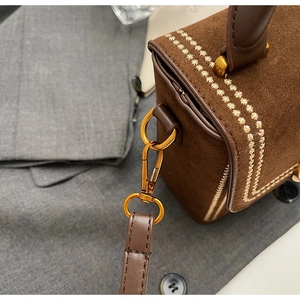 Vue macro du sac en daim marron avec broderie et détails métalliques dorés fins