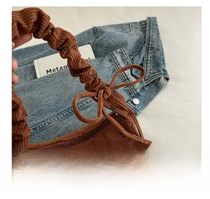 Detail of brown corduroy shoulder bag with black bow patterns and pleated handle