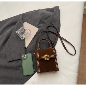 Petit sac en daim marron foncé avec boucle dorée et rivets dans une ambiance de mode chic