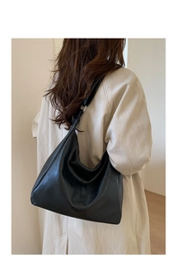 Close-up of minimalist black leather tote bag with wide strap and silver metal buckle on model
