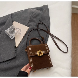 Gros plan d'un sac en daim marron avec fermoir doré et surpiqûres sur une veste grise