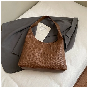 Dettaglio di una borsa hobo intrecciata marrone con ampia tracolla su tessuto bianco